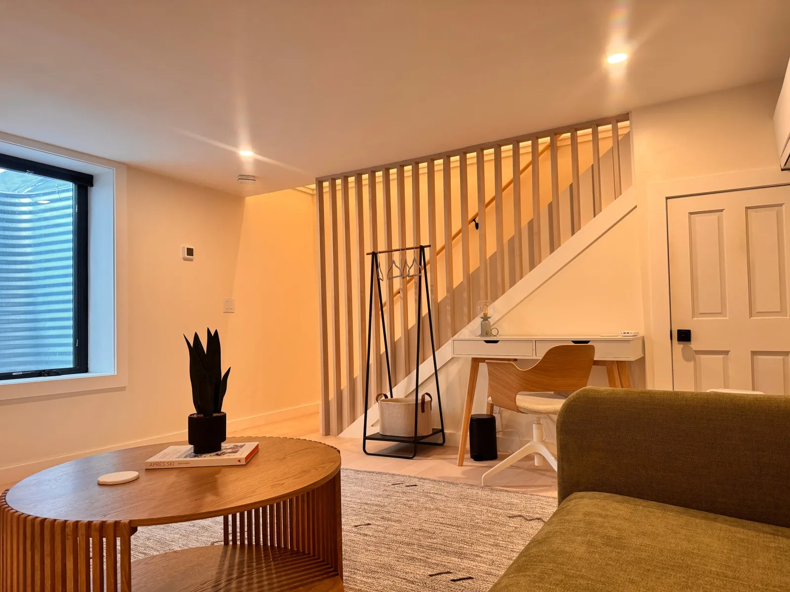 Lower-level lounge with a green sofa, round oak table and slatted stair screen