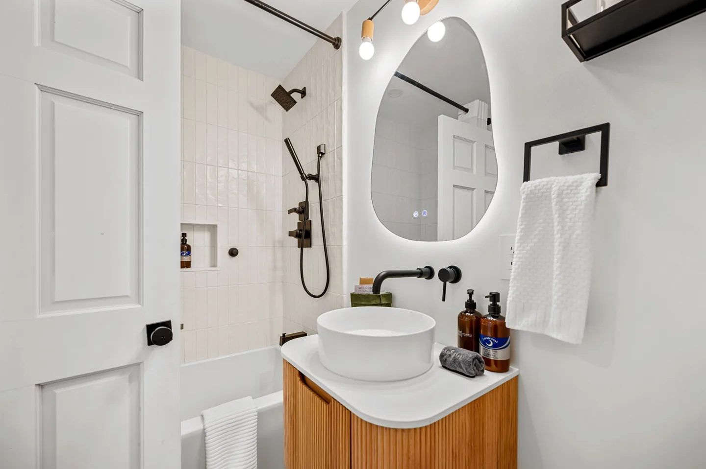 Fully renovated guest bathroom at a Stowe vacation rental with a deep soaking tub, tiled shower with overhead head and handheld wand, fluted oak vanity and a backlit mirror