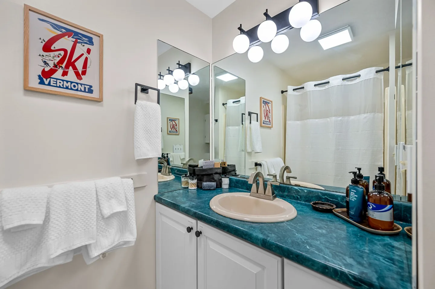 Primary en-suite bathroom with a long vanity, wide mirror, globe lighting and a framed Vermont ski poster
