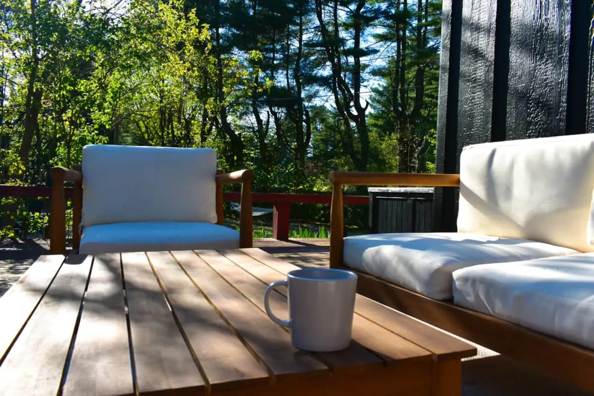 Deck with teak lounge seating and a coffee mug under tall pines