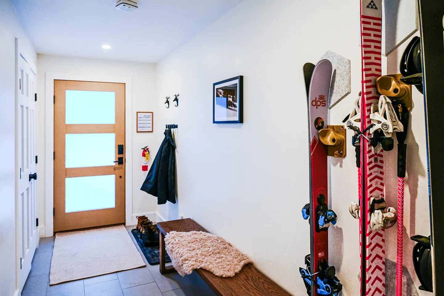 Bright tiled entry with a wood-framed glass front door, bench with a sheepskin throw, boot tray, coat hooks and wall-mounted ski racks