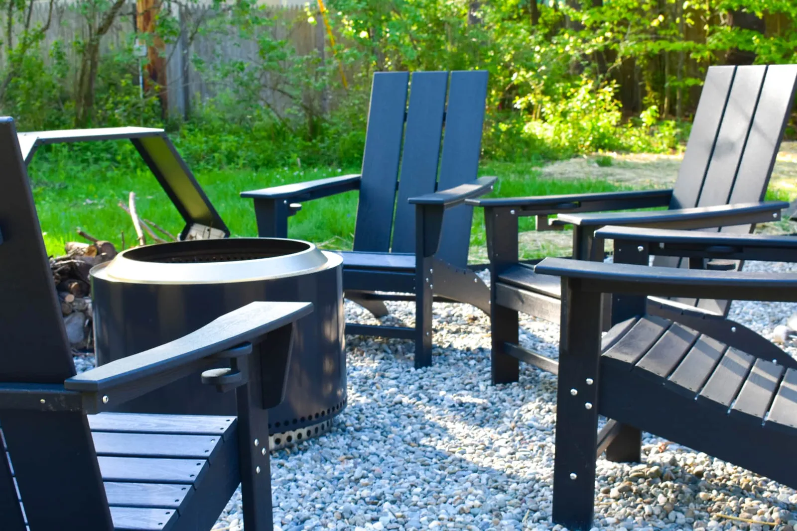 Solo Stove fire pit ringed by black Adirondack chairs on crushed stone