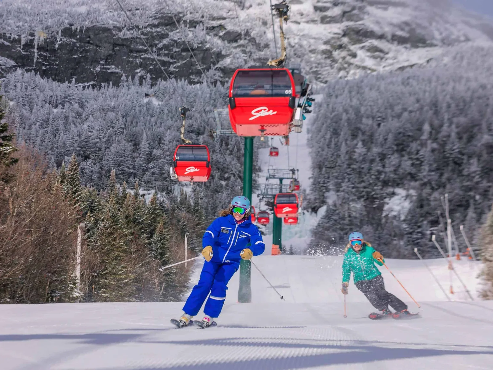 Skiers carving down a groomed trail beneath Stowe's red gondola