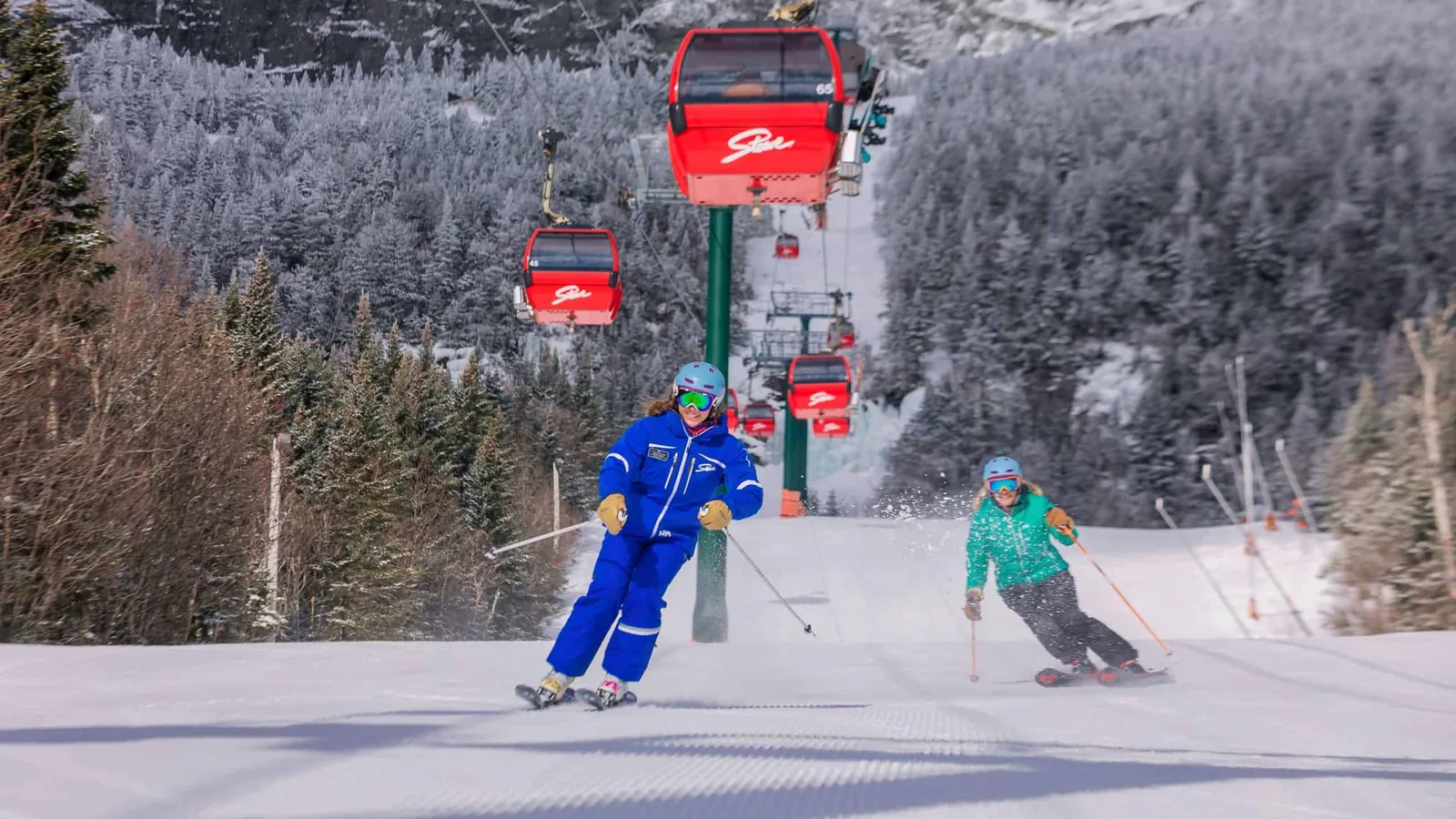 Skiers carving down a groomed trail beneath Stowe's red gondola