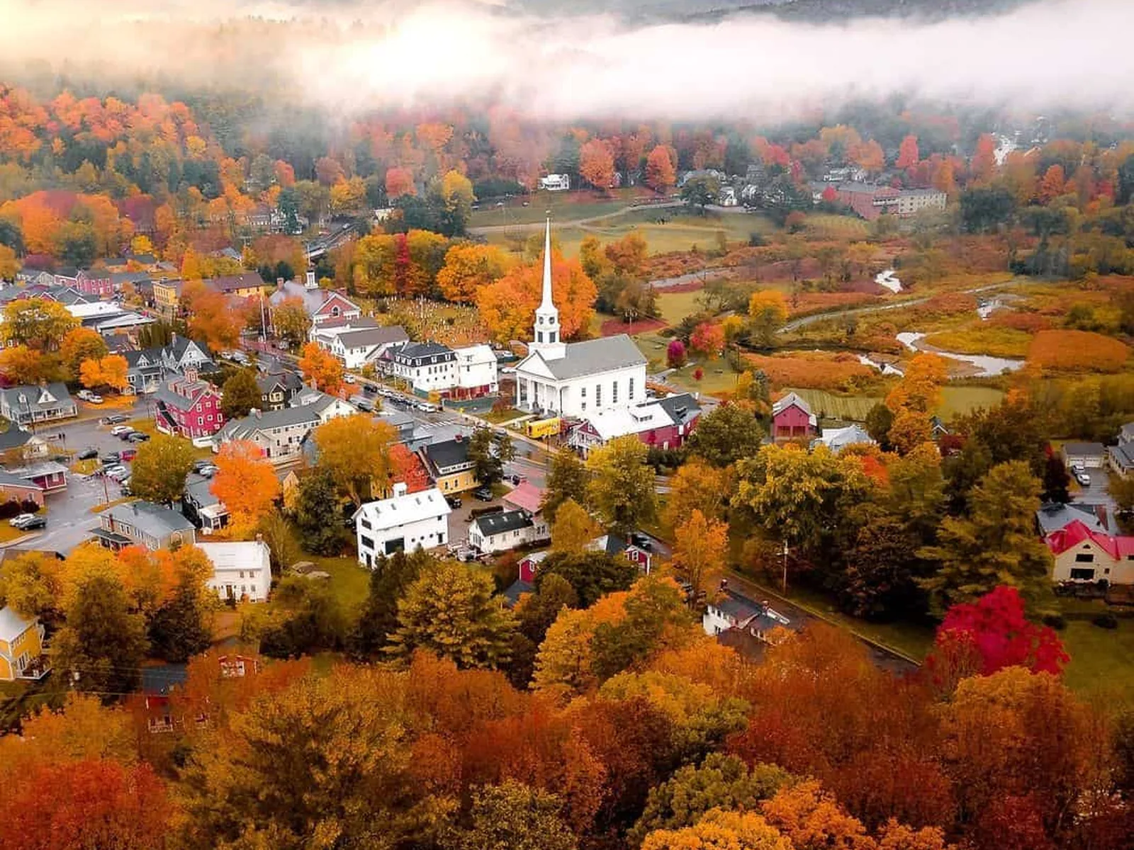 Aerial view of Stowe village and its white steepled church among fall color and morning fog